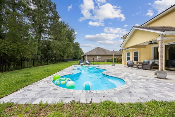 Un patio trasero con piscina, mobiliario de jardín y una casa.
