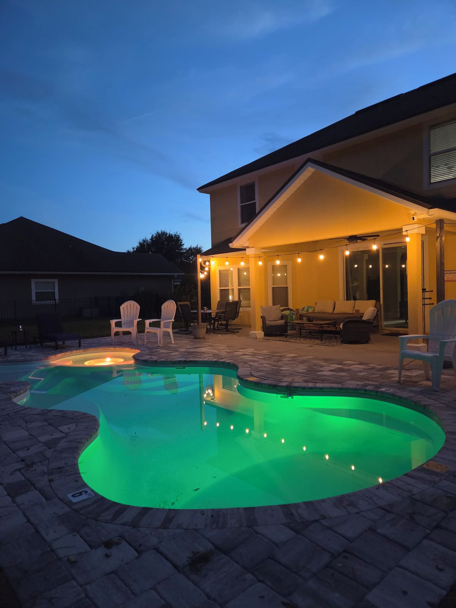 A backyard with a swimming pool, outdoor seating, and string lights.