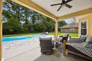 Un patio cubierto con piscina, mobiliario exterior y ventilador de techo.