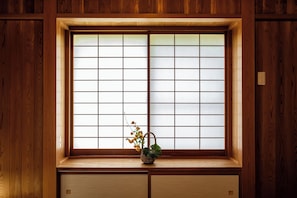 Ein traditioneller japanischer Raum mit einem Fenster aus Shoji-Papier, einer Holzbank und einem kleinen gewebten Korb mit Blumen.