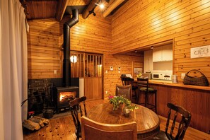 Ein Holzinnenraum mit Kamin, einem Esstisch mit Stühlen und einer Küchenzeile.