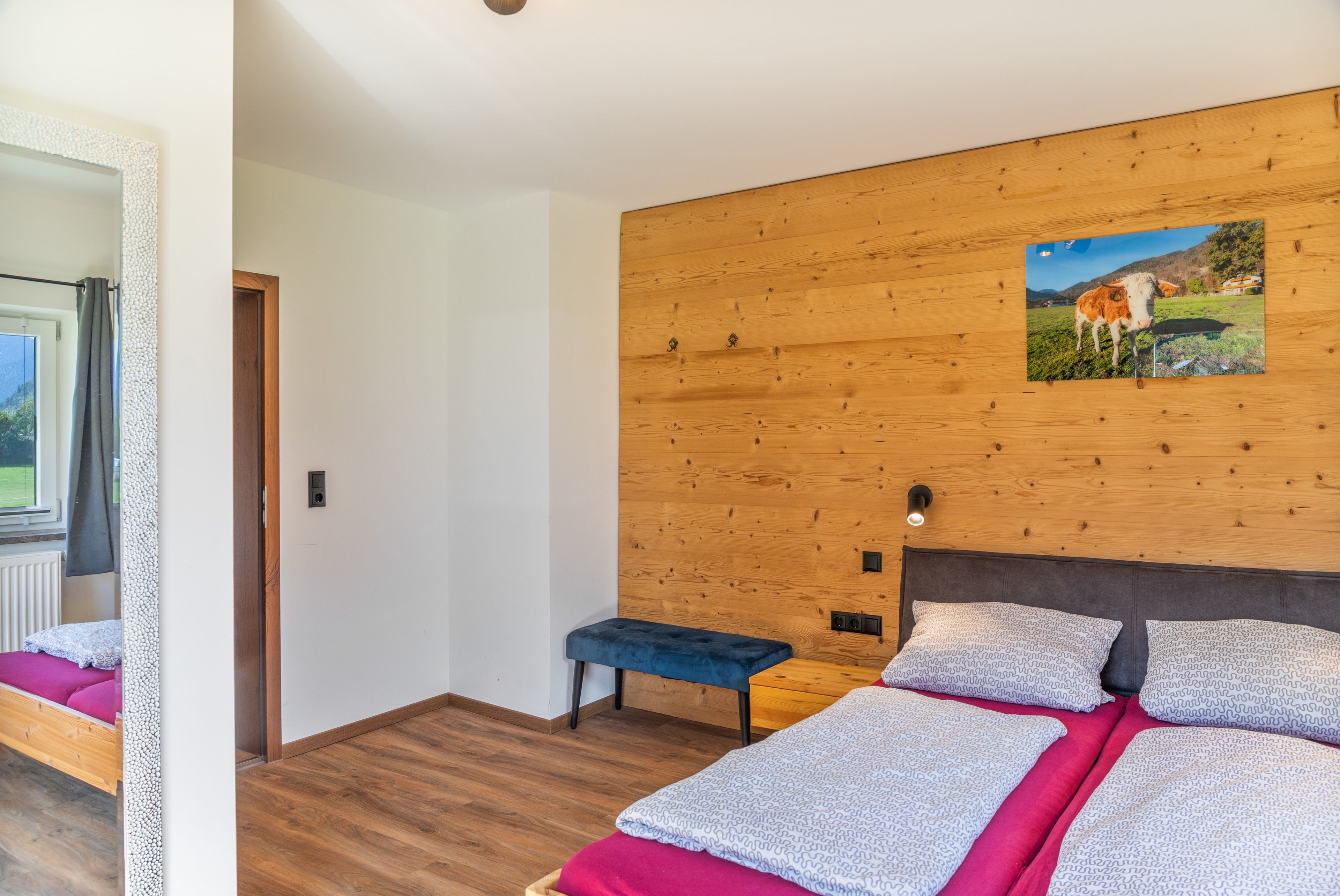 A bedroom with a wooden headboard, a bed with patterned bedding, a bench, and a wall-mounted picture.