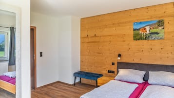 A bedroom with a wooden headboard, a bed with patterned bedding, a bench, and a wall-mounted picture.