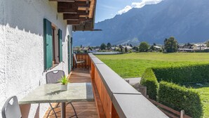 En balkon med et bord og en stol, der kigger ud over en grøn mark og bjerge.