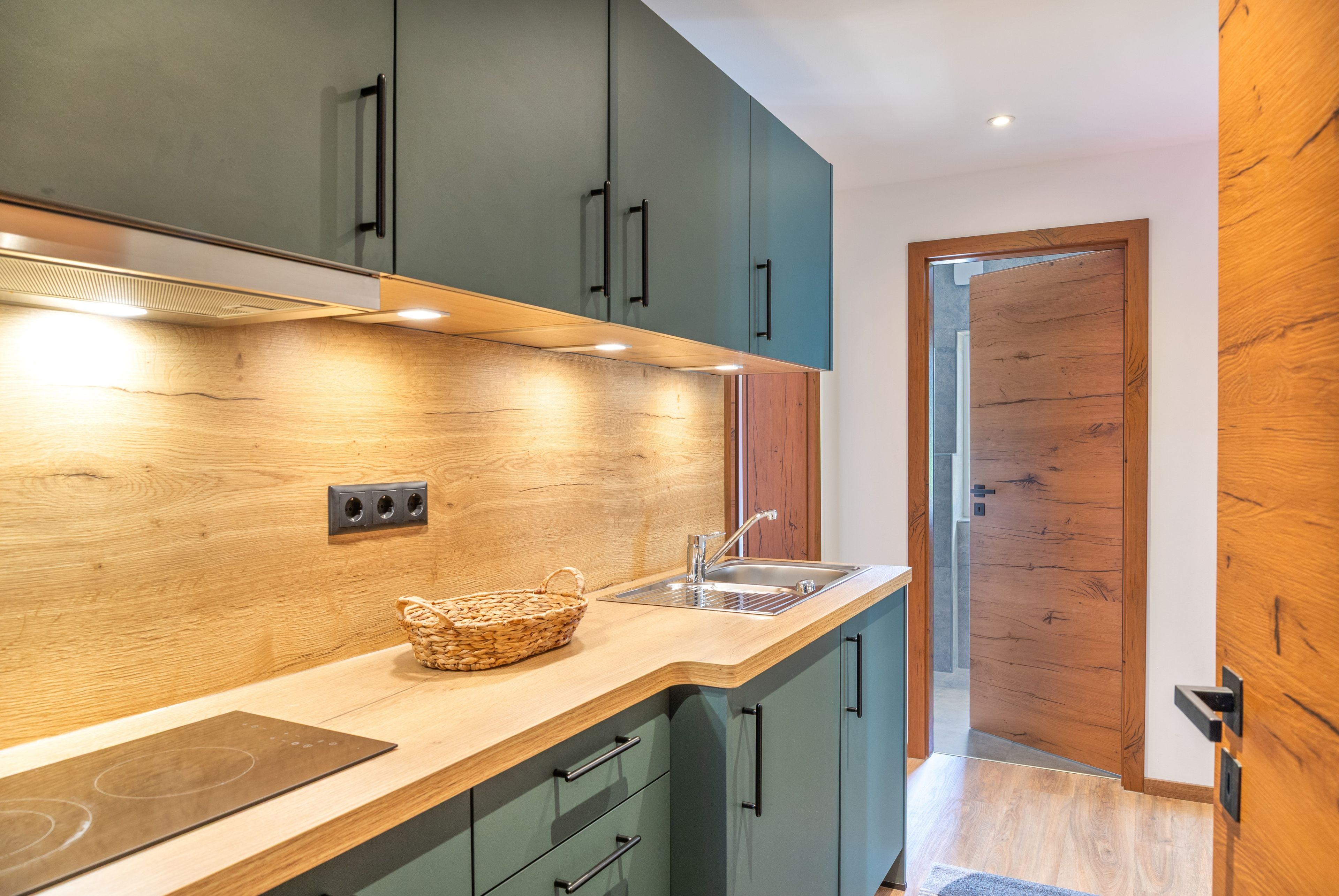 Une cuisine moderne avec des plans de travail en bois, des armoires vertes et une cuisinière intégrée.