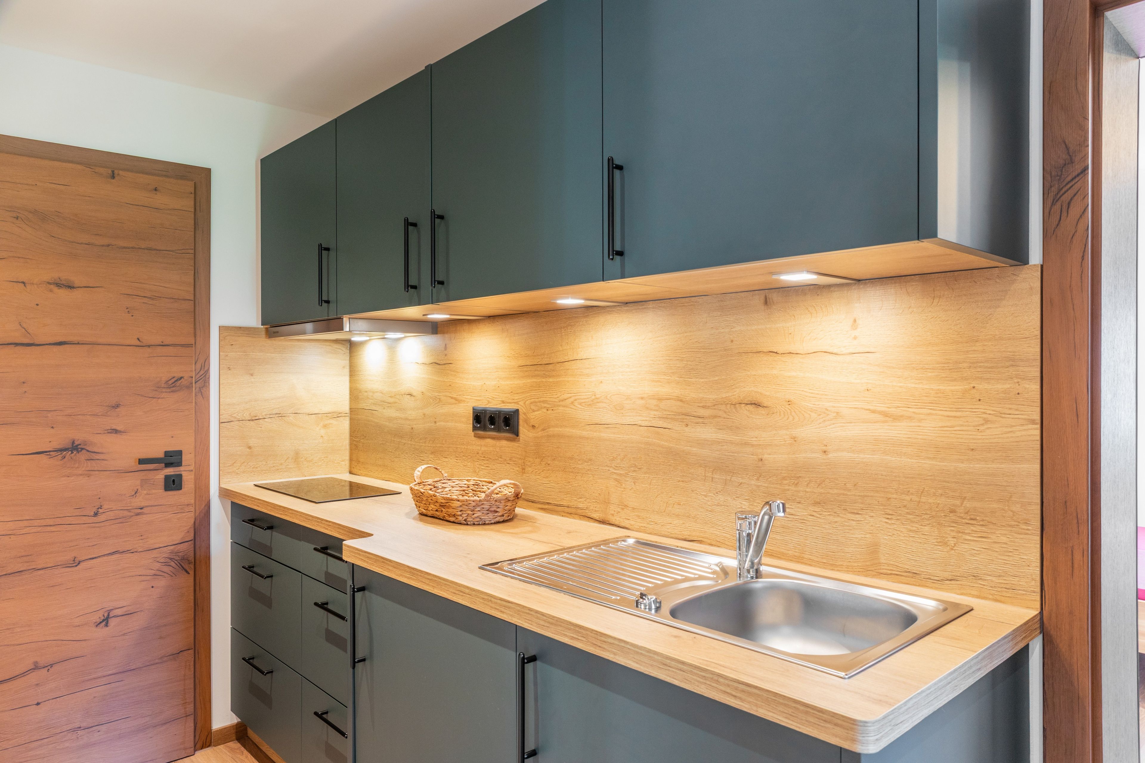 Eine moderne Küche mit Holzschränken, einer Edelstahl-Spüle und einer Unterbauleuchte.