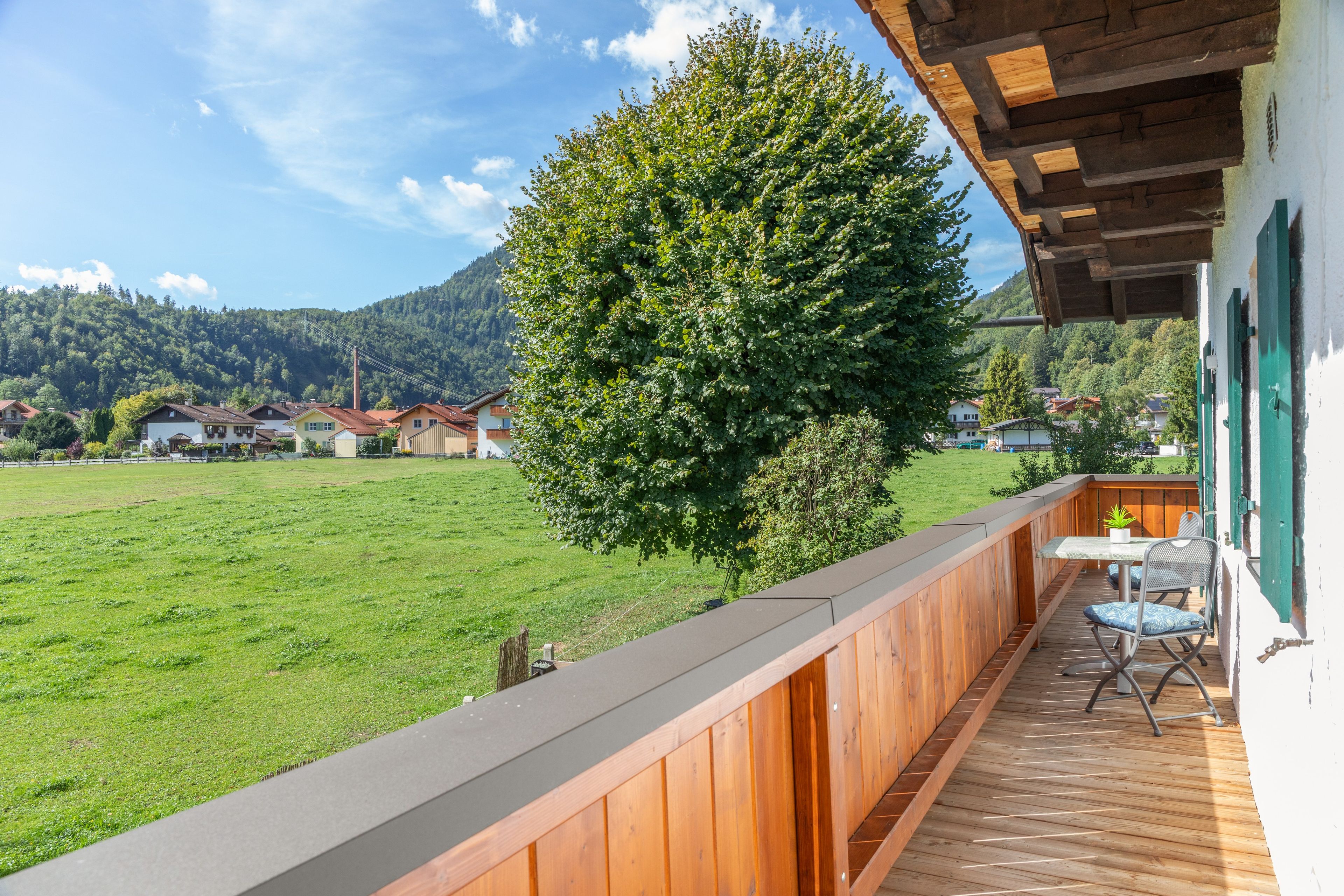 Eine Holzterrasse mit Blick auf ein grünes Feld und Häuser im Hintergrund.