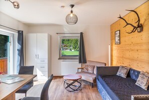 Een modern interieur met een houten wand, een bank, een eettafel en uitzicht op een groen landschap door een raam.