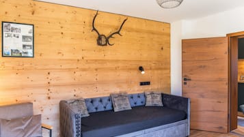 A modern interior with a wooden wall, a mounted antler, a framed photo collage, a sofa with decorative pillows, and a door.