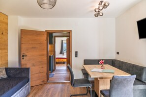 A modern interior with a wooden door, a dining area with a table and chairs, a grey sofa, and a TV mounted on the wall. - Apartment "Ferienwohnung Schulerhof" with Mountain View, Balcony and Wi-Fi (Oberau)