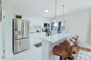 A modern kitchen with white cabinetry, stainless steel appliances, and a central island with bar stools.