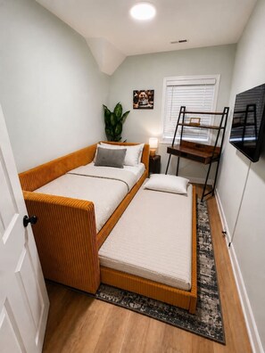 Une petite chambre comprenant un lit, un petit bureau, une plante et un téléviseur.