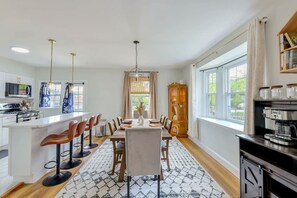 A modern kitchen with a dining area, large windows, and a coffee machine.