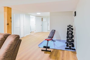 A room with a bench, a set of dumbbells, and a yoga mat on the floor.