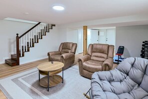 A living room with a staircase, two leather armchairs, a grey sofa, and a small round table.