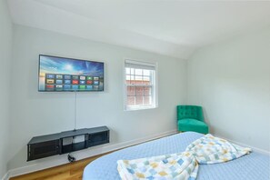 A bedroom with a bed, a TV mounted on the wall, a window, and a green chair.