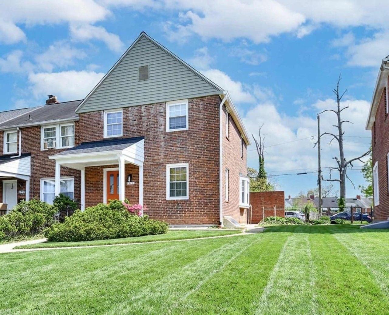A two-story brick house with a front porch, a well-maintained lawn, and a clear sky.