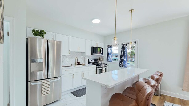 A modern kitchen with white cabinetry, stainless steel appliances, a central island with bar stools, and pendant lighting. - The Coffeehouse - King Bed - Gym - Fast WiFi - Full Kitchen - Great Vibes (Baltimore)