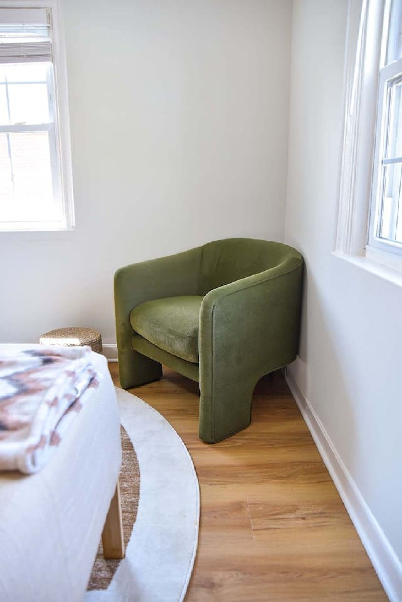 A corner room with a green armchair, a round white rug, and a bed with a floral bedspread.