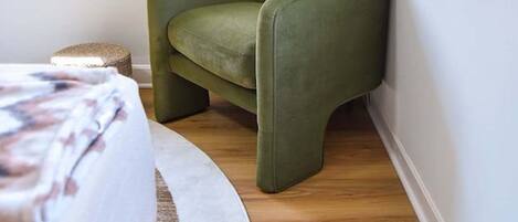 A corner room with a green armchair, a round white rug, and a bed with a floral bedspread.