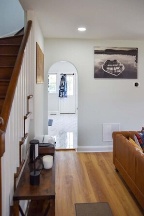 Un interior moderno con una escalera de madera, una sala de estar con un sofá marrón, una cocina con armarios blancos y un comedor con una mesa y sillas.