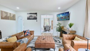 A living room with a sofa set, a coffee table, a TV, and a dining area in the background. - The Coffeehouse - King Bed - Gym - Fast WiFi - Full Kitchen - Great Vibes (Baltimore)