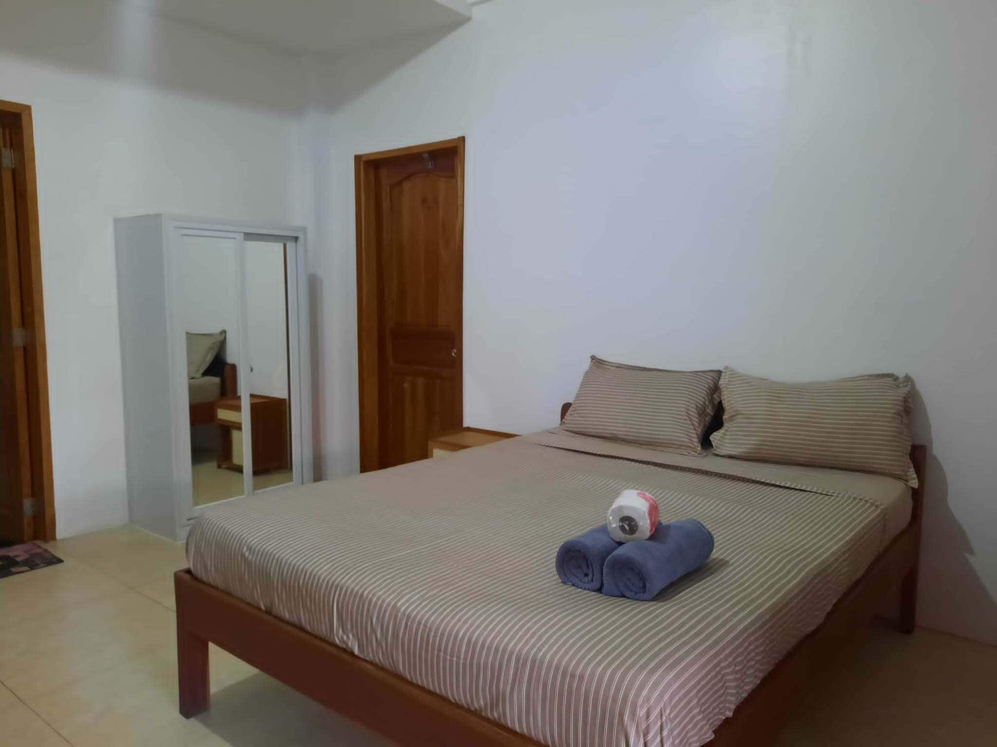 A bedroom with a bed, two wooden doors, a mirror, and a small table.