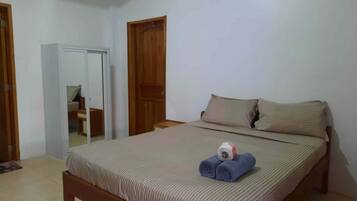 A bedroom with a bed, two wooden doors, a mirror, and a small table.