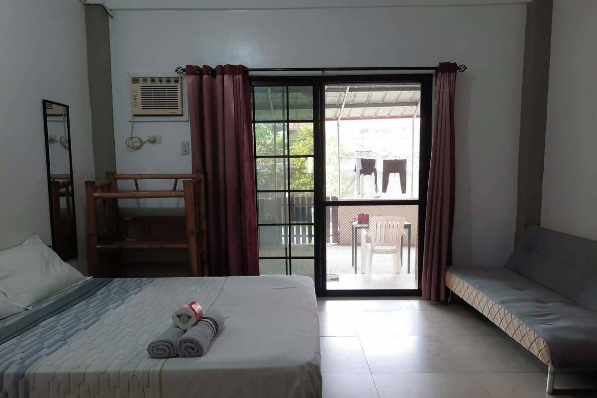 Una habitación con una cama, un sofá, una silla de madera, una mesita y un ventanal corredero que da a un espacio al aire libre.