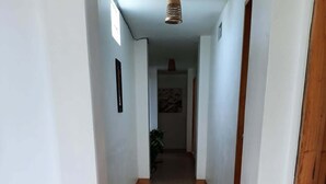 Un pasillo con paredes blancas, piso de madera y una lámpara colgante.