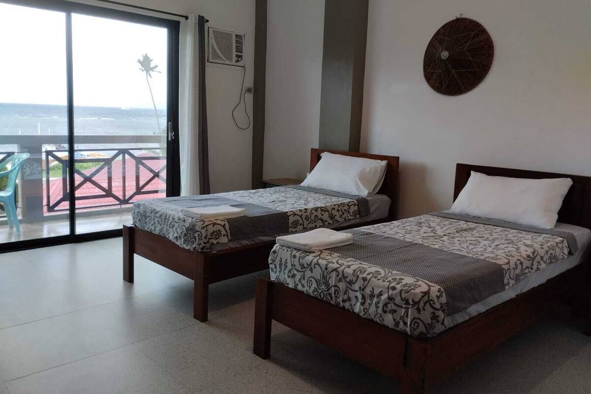 Habitación de hotel con dos camas, un amplio ventanal corredero al exterior, una mesita y un aire acondicionado de pared.