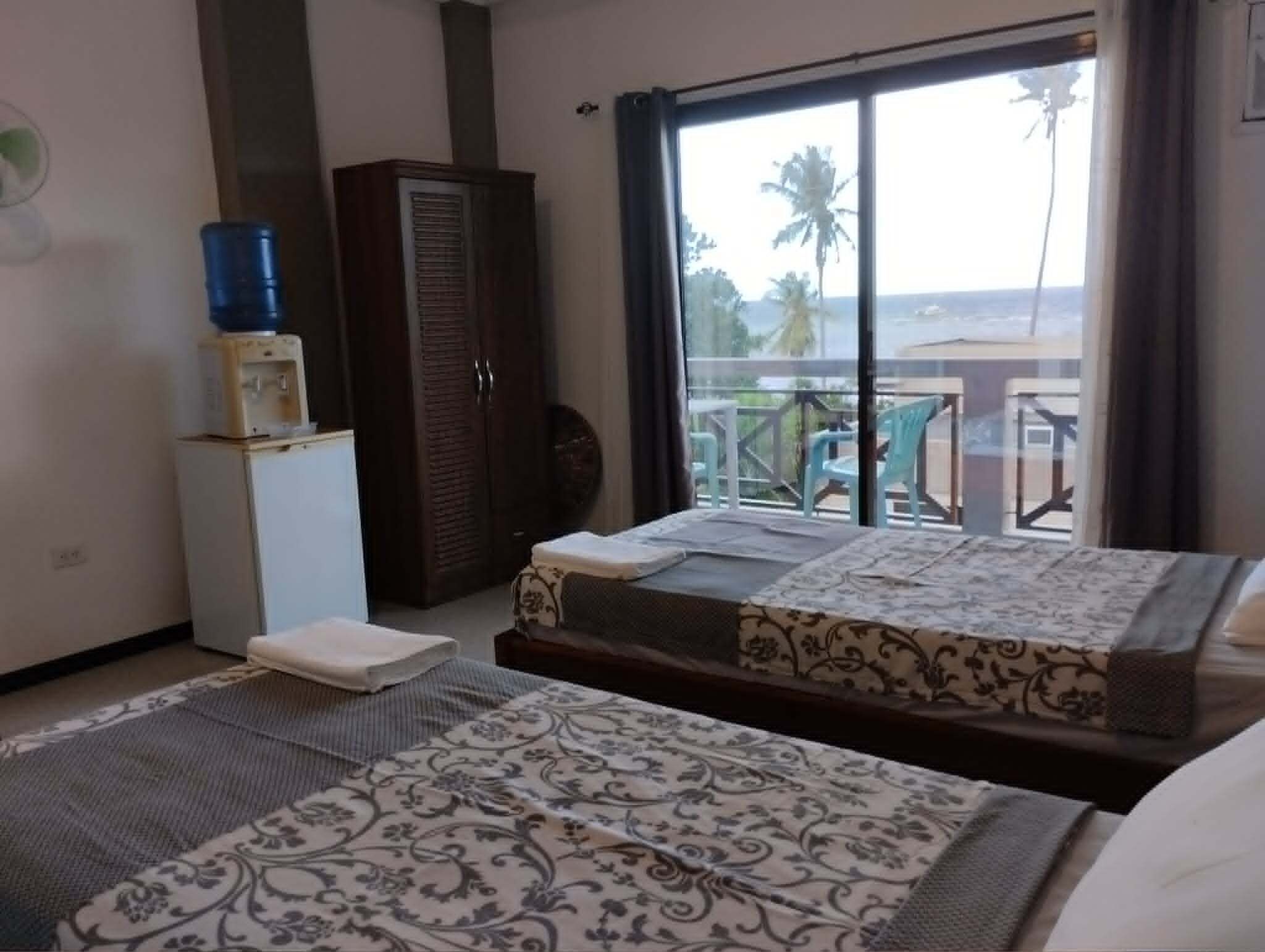 A hotel room with a bed, a wardrobe, a small fridge, a water dispenser, and a balcony with a view.