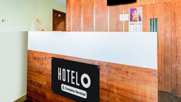 Un comptoir d’accueil d’hôtel avec une pancarte indiquant « Service assuré par HOTELO Company », une caméra de surveillance, un téléviseur et un calendrier.