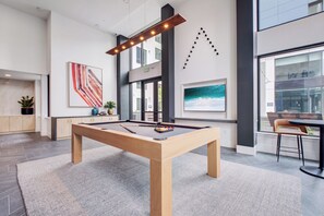 Una mesa de billar en una habitación moderna con un ventanal grande, arte abstracto y vistas al exterior.
