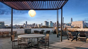 A rooftop patio with a round table and chairs, a pergola, and a city skyline view. - Premium 1-bedroom apartment with Gym &Work Desk (San Francisco)