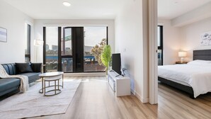 A modern hotel room with a bed, a sofa, a small table, and a large window offering a city view. - Premium 1-bedroom apartment with Gym &Work Desk (San Francisco)