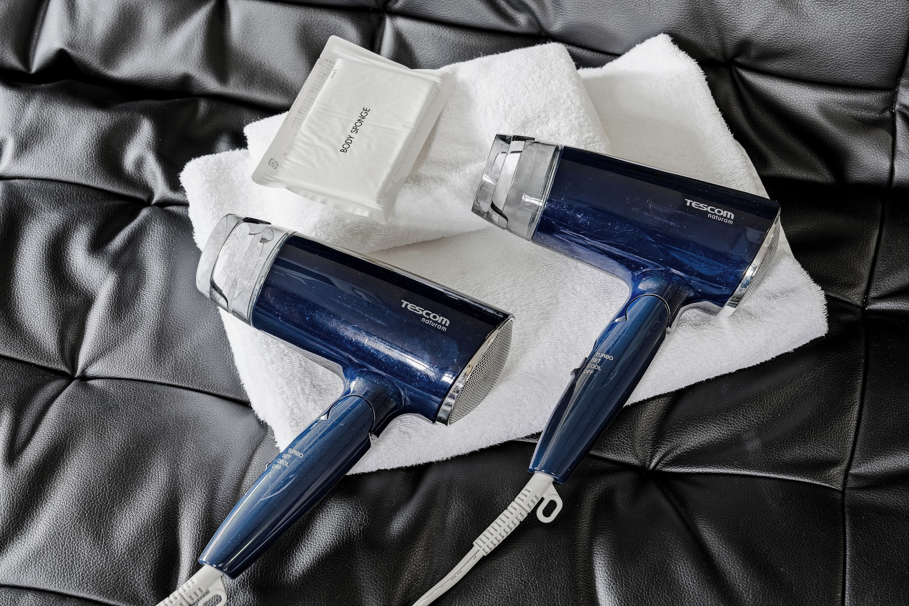 Two blue hairdryers and a white box on a black leather couch.