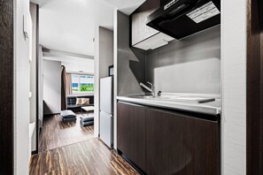 A modern kitchen with a built-in sink, dark wood cabinets, and a window overlooking a green outdoor area. - MJ STAYS (Sapporo)