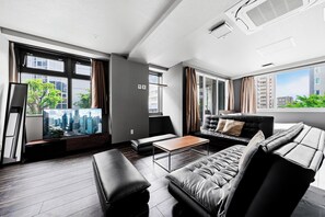 Una sala de estar moderna con un televisor de pantalla plana grande, sofás de cuero, una mesa de centro de madera y ventanas amplias con cortinas.