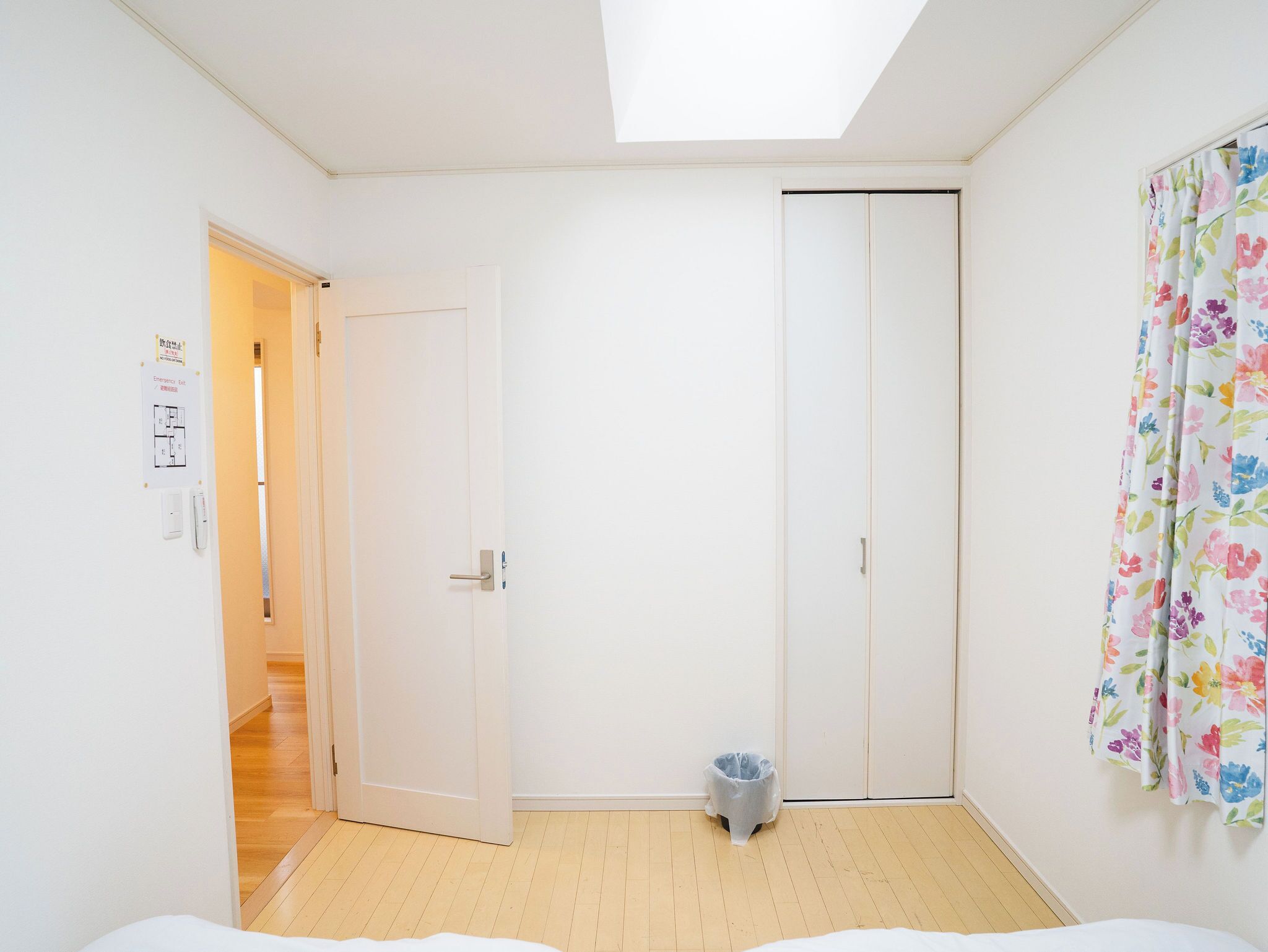Een kamer met dakraam, een kledingkast, een prullenbak en een deur naar een andere kamer.