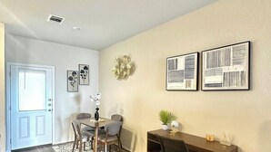 A room with a wooden floor, a dining table with chairs, a desk with a chair, and wall-mounted artwork. - [HB102] New 3BR near JBSA, Randolph Airforce Base I Fully Stocked + Parking (San Antonio)