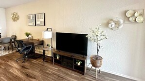 A living room with a flat-screen TV, a dining table, chairs, a coffee table, a lamp, and decorative items on the wall. - [HB102] New 3BR near JBSA, Randolph Airforce Base I Fully Stocked + Parking (San Antonio)