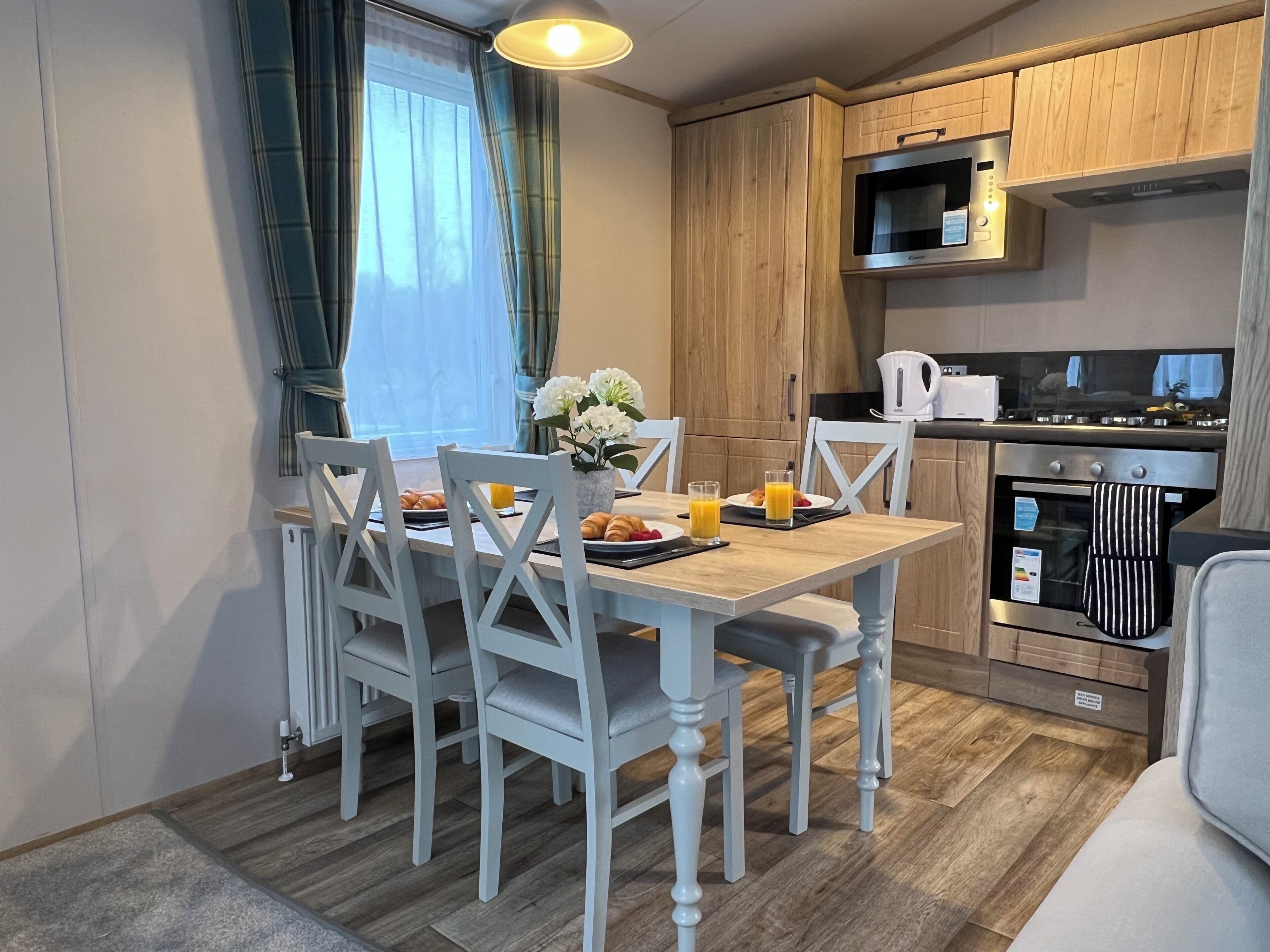 A compact kitchen with wooden cabinets, a microwave, an oven, and a dining table with chairs.