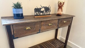 A wooden console table with two drawers and a shelf, a potted plant, and a decorative cow figurine.