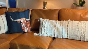 A brown leather sofa with decorative pillows, a wall-mounted lamp, and a framed artwork of a bull.