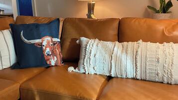 Un canapé en cuir marron agrémenté de coussins décoratifs, une lampe fixée au mur et une œuvre d’art encadrée représentant un taureau.