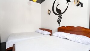 Ett rum med två enkelsängar, en sänggavel i trä, en väggdekor i form av en halvmåne och en liten vägglampa.