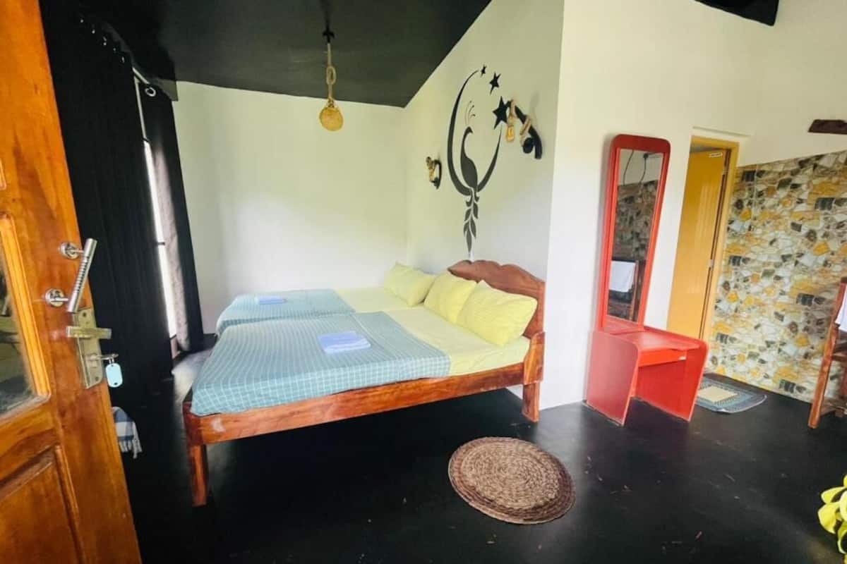 A bedroom with a wooden bed, a small red chair, a woven mat, a wall decoration, and a mirror.