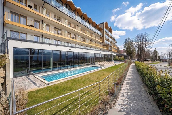 Ein modernes Gebäude mit Schwimmbad, mehreren Balkonen und einem gepflasterten Weg.