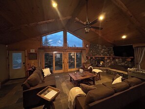 Ein gemütliches Wohnzimmer mit Kamin aus Stein, Holzboden und einem großen Fenster mit Blick auf ein Gebäude.